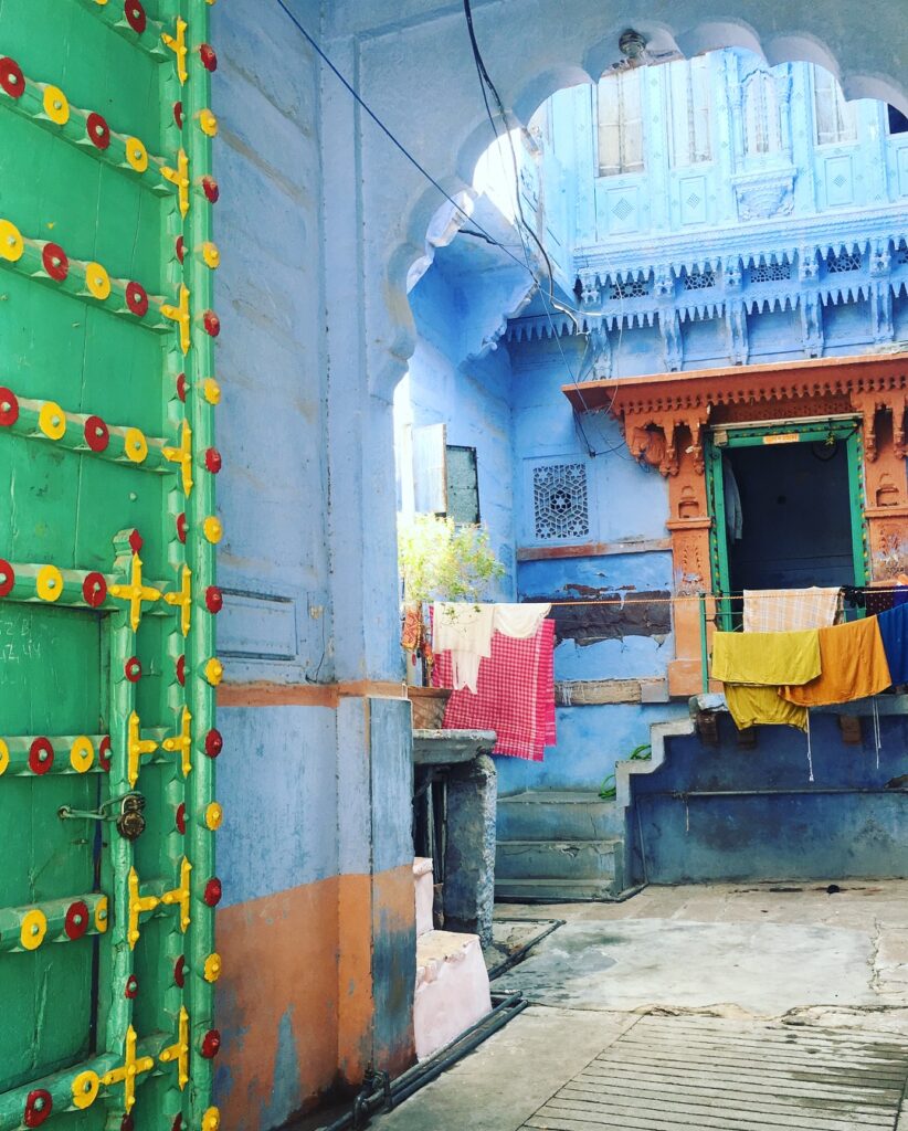 Doorway in Jodhpur's old town with green door accented with yellow and red dots and a clothes hanging with colorful towels inside an arched entryway.