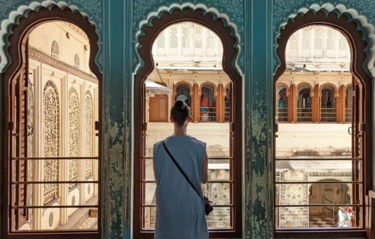 The back of a girl in blue dress standing in the middle of three scalloped archways painted blue inside the City Palace in Udaipur.