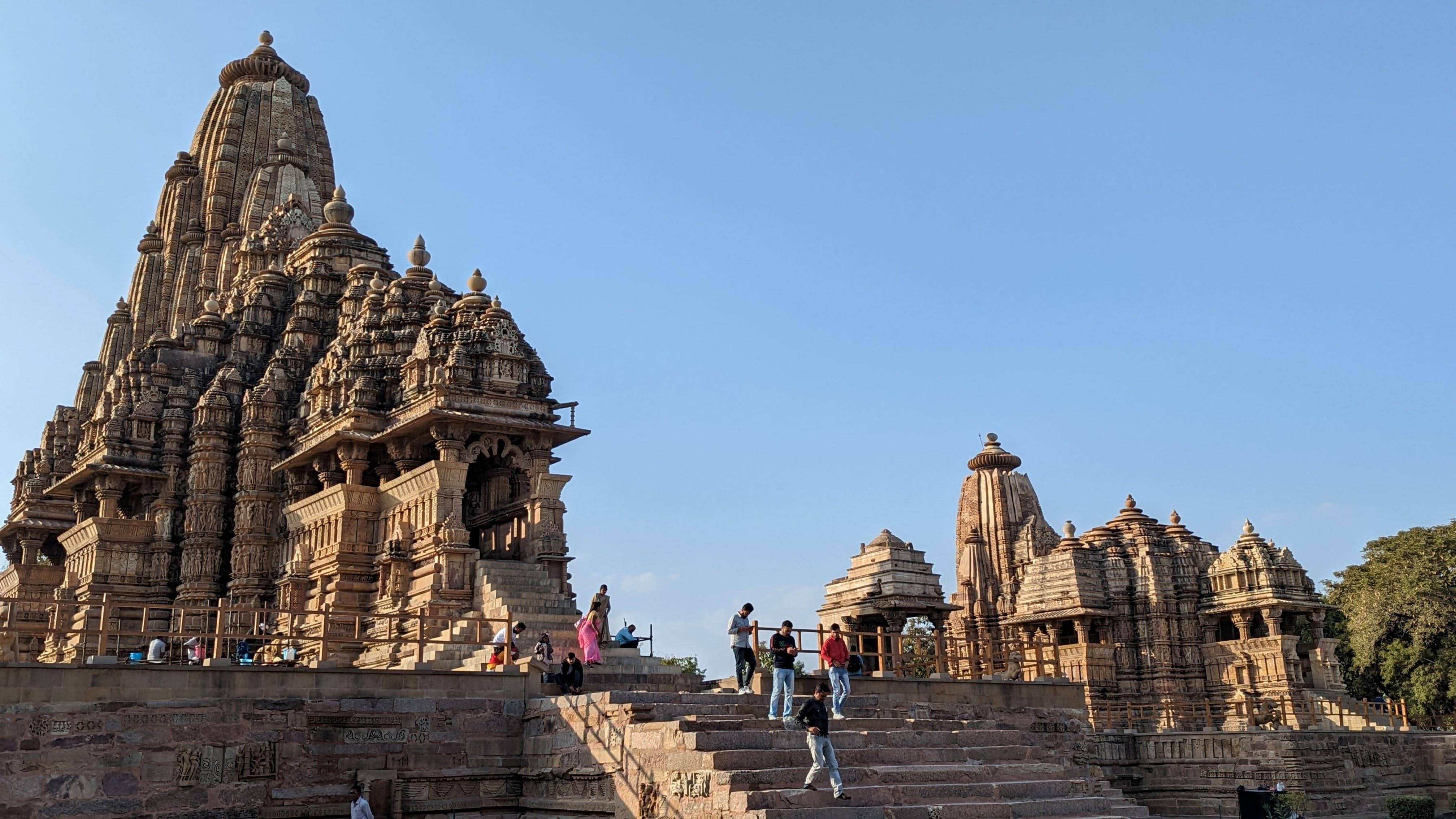 View of 2 temples at the western block of Khajuraho Temples. Each temple is intricately carved with sculptures along the outside the walls.