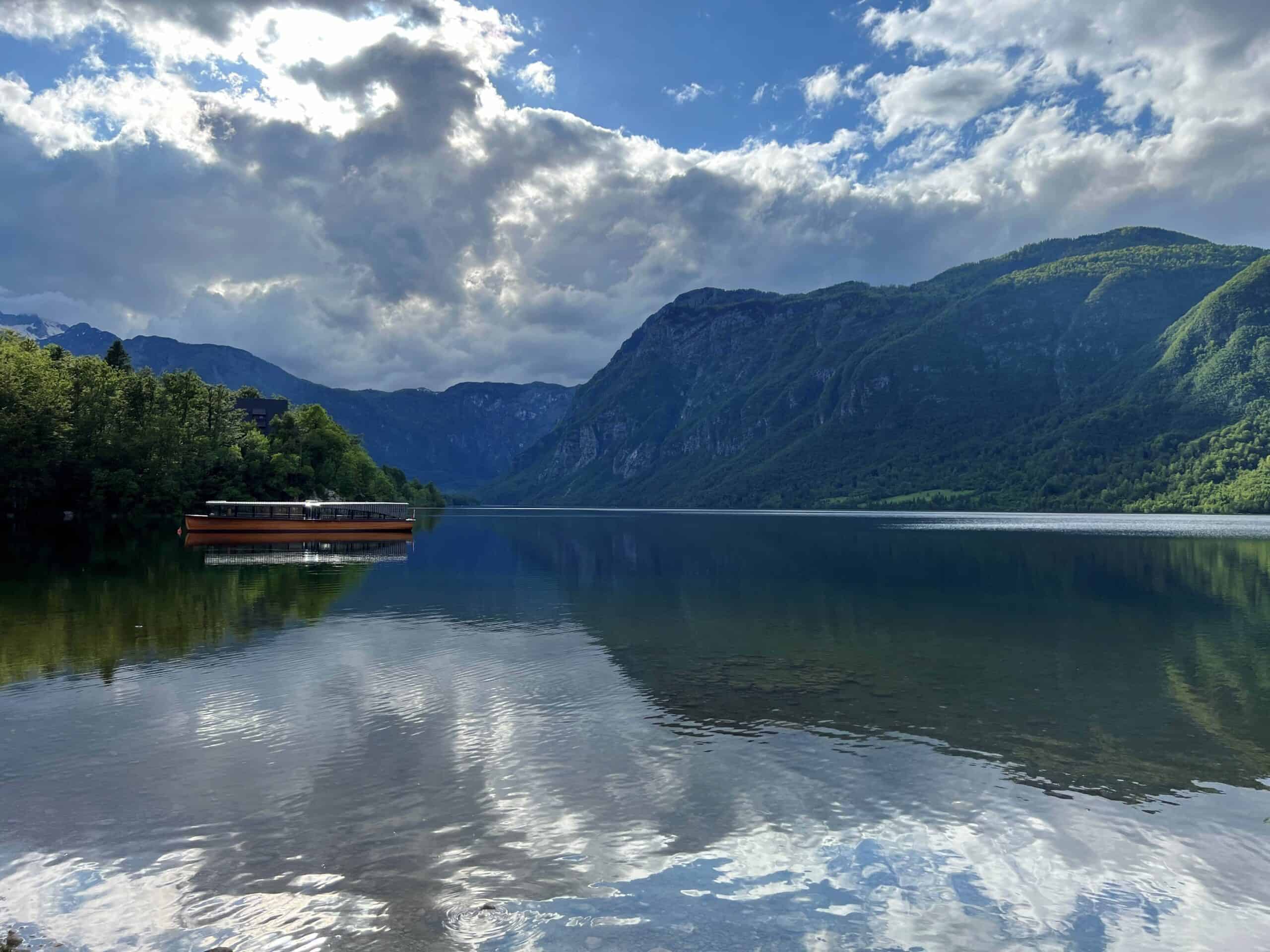 Wide view of Lake Bohinj at dusk with a wooden boat in the water and the alps in the background.