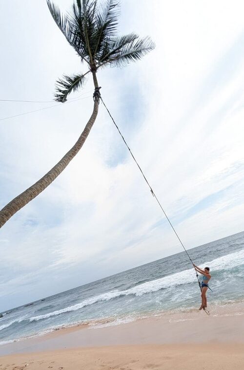 Girl swinging on rope swing hanging from a palm tree on the beach