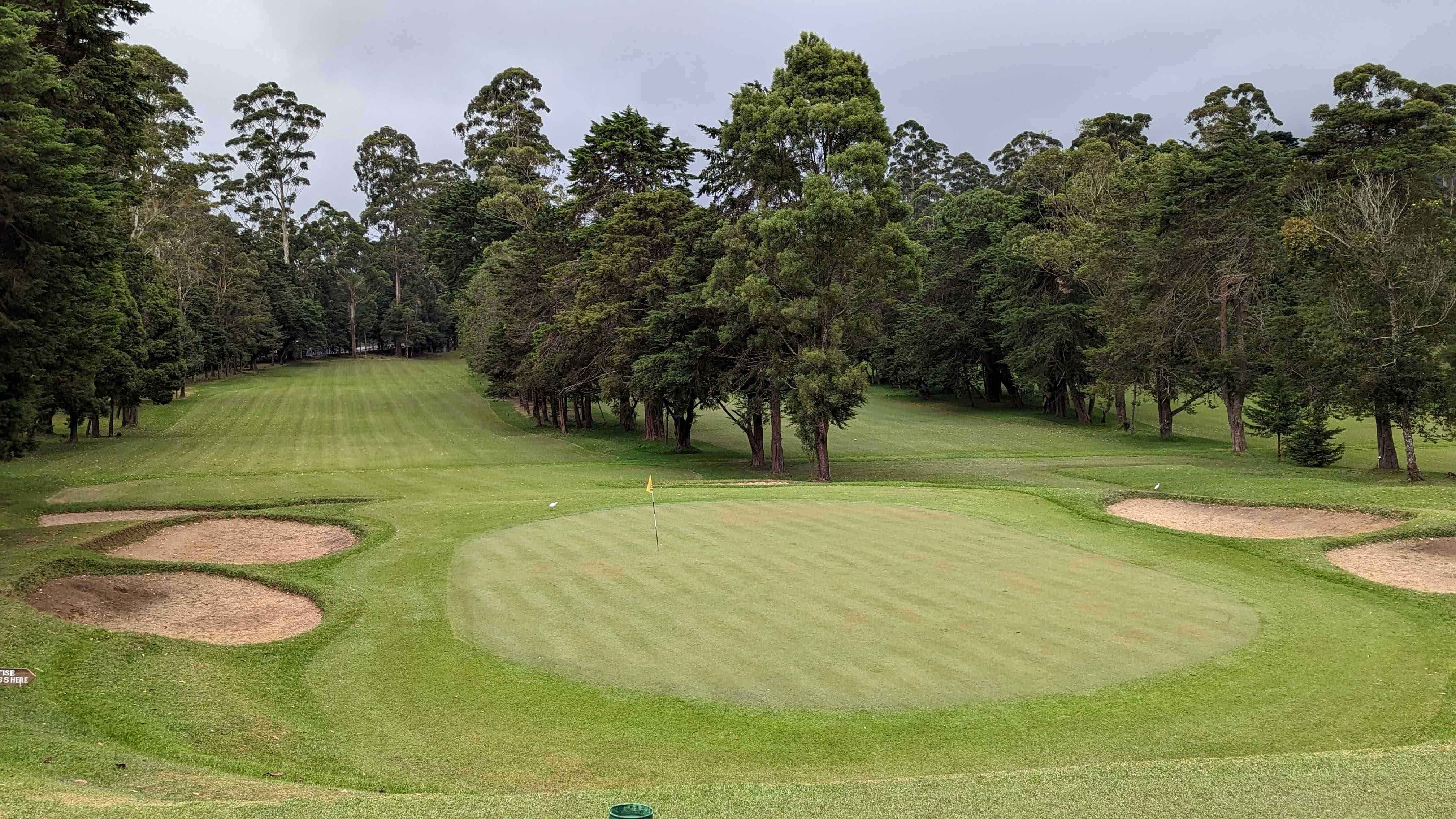 View of the golf green and a couple sand traps at Nuwara Eliya Golf Club on a cloudy day.