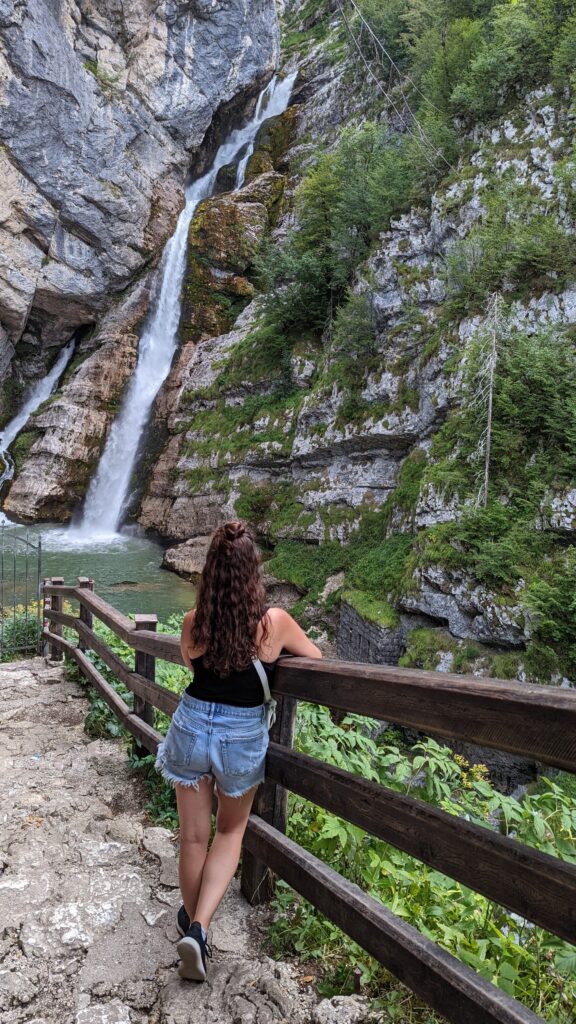 A girl's back as she looks at Slap Savica waterfall in Bohinj, a must do short hike when visiting Lake Bled for one day