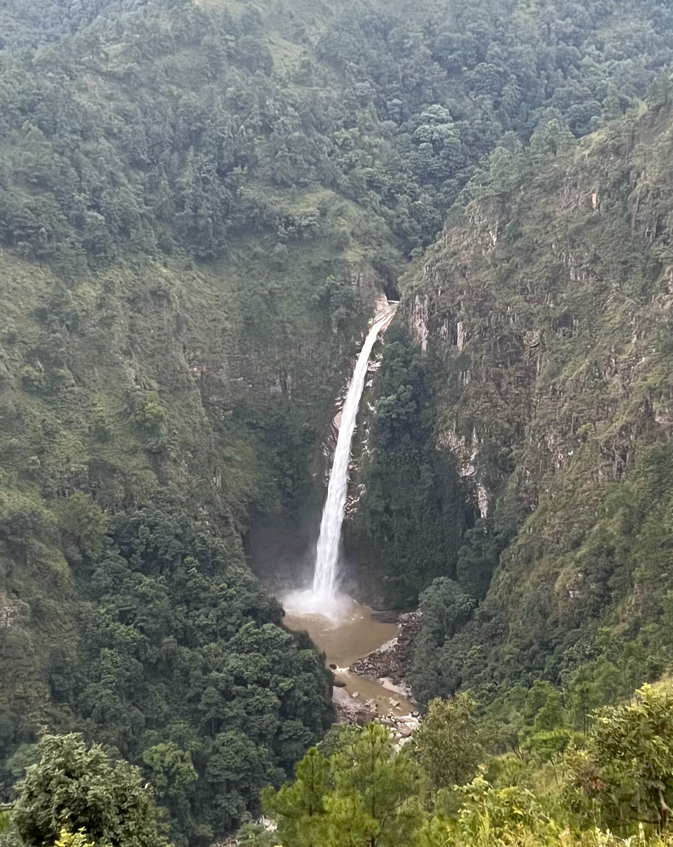 View of Sweet Falls in Shillong, with the single stream waterfall in the center surrounded by the green rocky landscape.