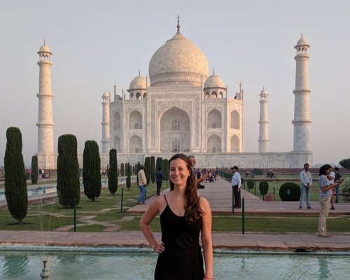 A girl in black dress standing in the gardens in front of the Taj Mahal in the early morning light.