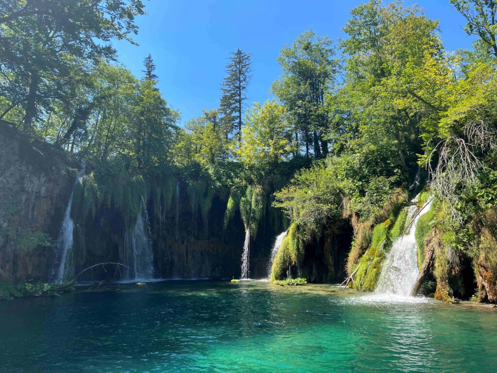 Five streams of waterfalls  flowing into a bright blue lake in the Upper Lakes section of Plitvice Lakes National Park in Croatia.