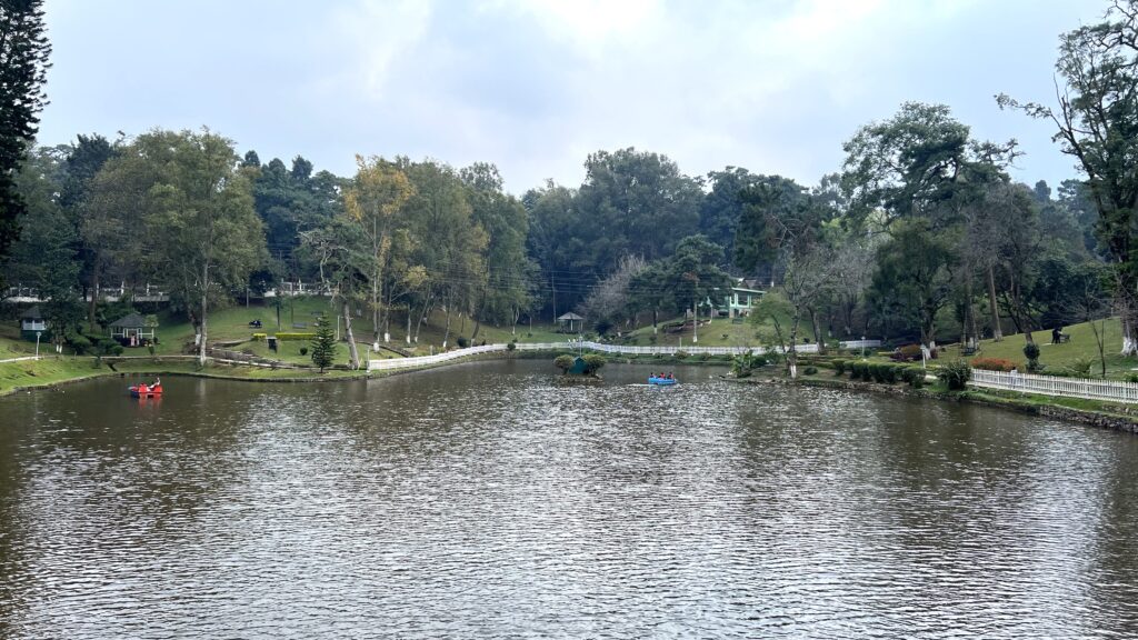 Ward's Lake in Shillong with the lake in the foreground and the bridge and park in the background. A couple paddle boats in the lake.