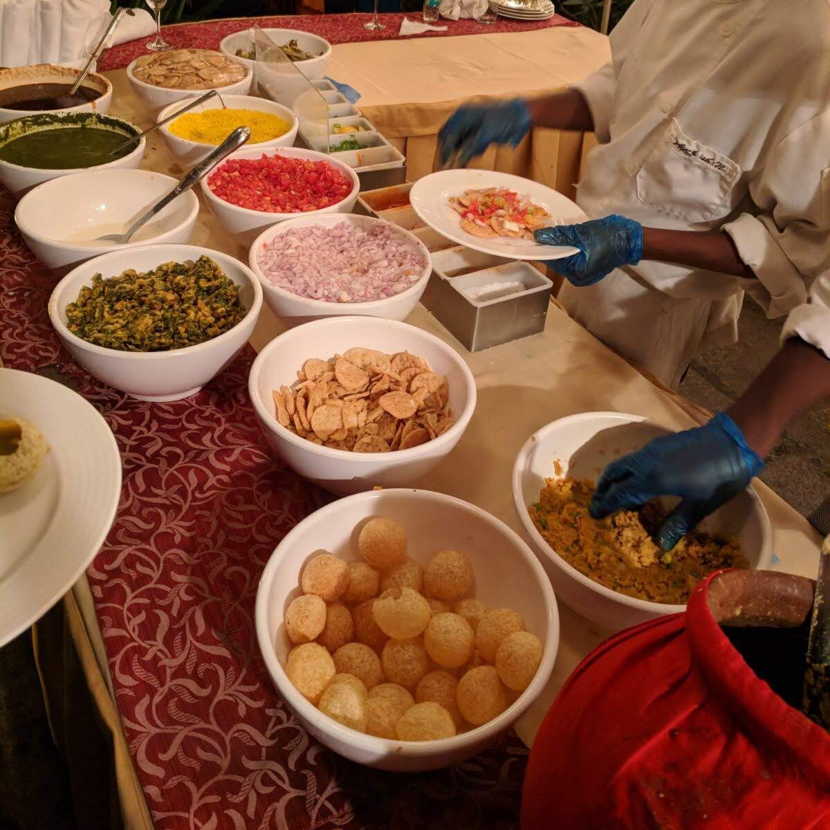 Overhead view of a chaat counter showing a variety of Indian food dishes in bowls including Pani Puri and more