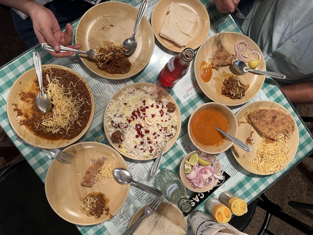 An overhead table shot of Berry Pulao and other dishes on a checkered table cloth at Cafe Britannia & Co, an iconic Parsi cafe in Mumbai