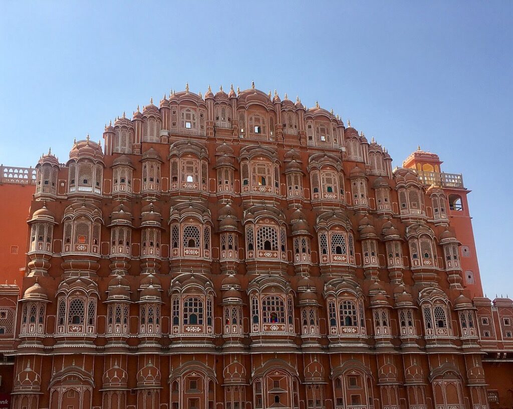 The intricate pink and white front facade of the Hawa Mahal in Jaipur, against a blue sky