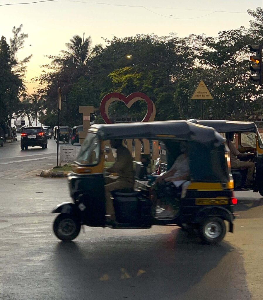 Auto rickshaw driving by on the streets of Bandra West in Mumbai with trees and sunset in the background.