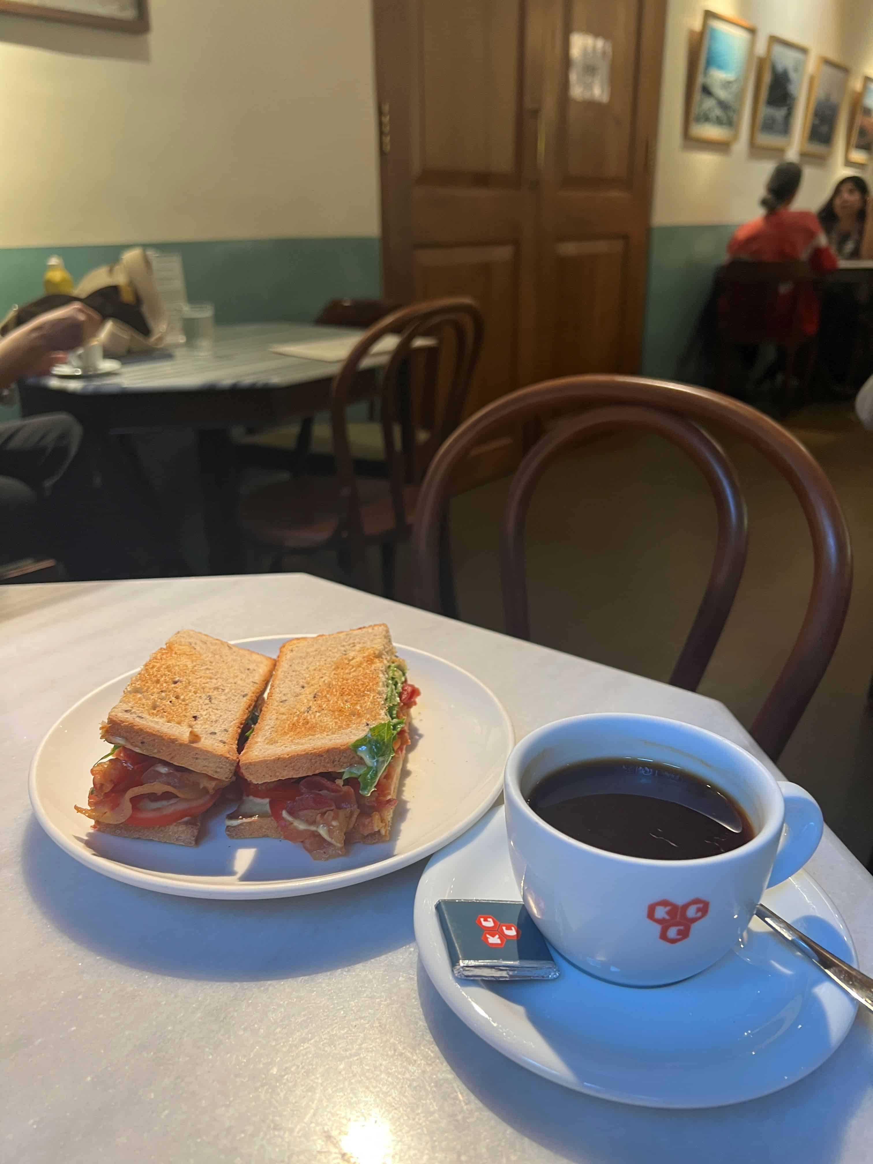 Close up of a BLT sandwich and coffee on a table at Kala Ghoda cafe.