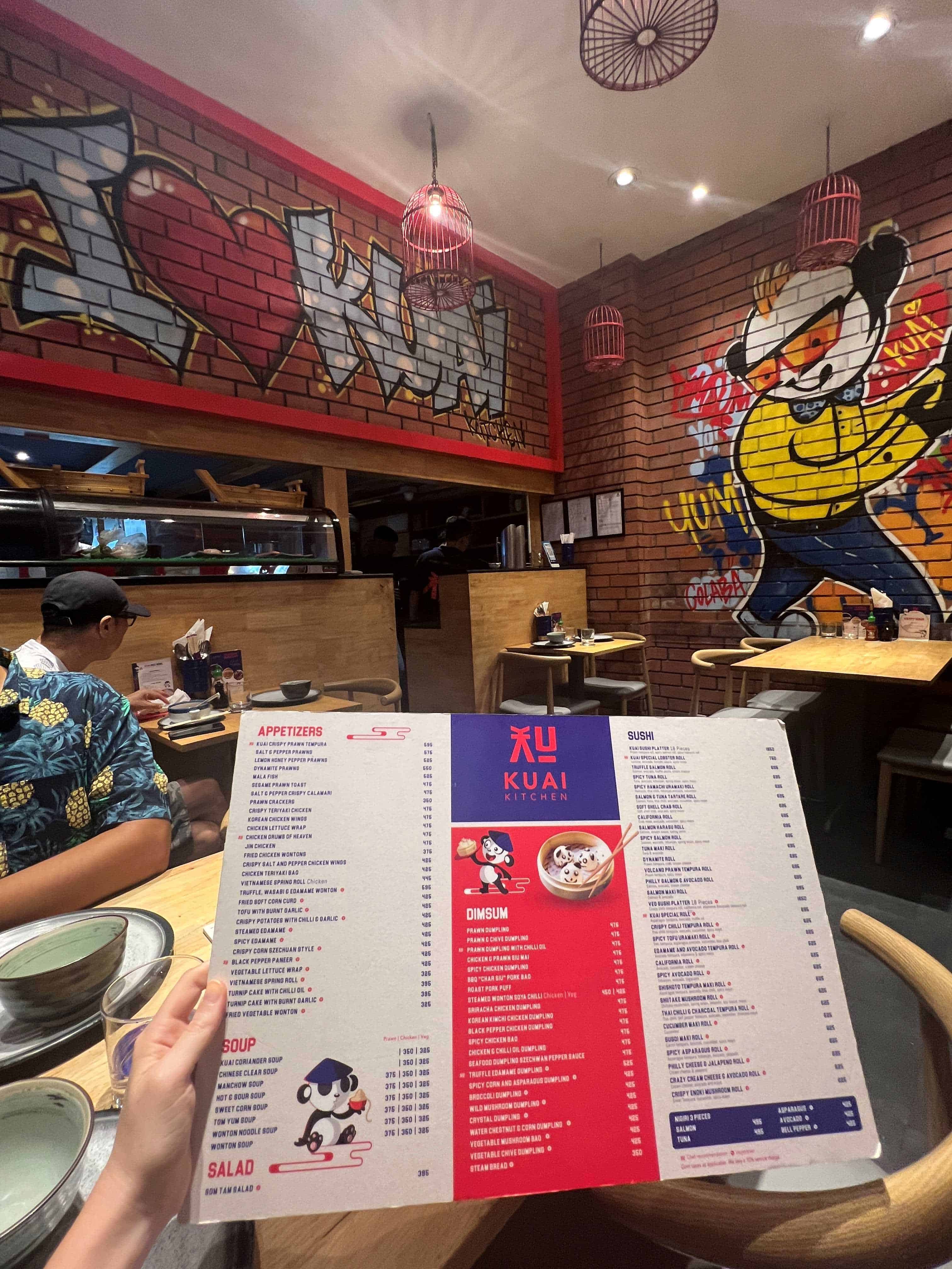 Menu being held over a table at Kaui Kitchen restaurant with graffiti brick walls in the background.