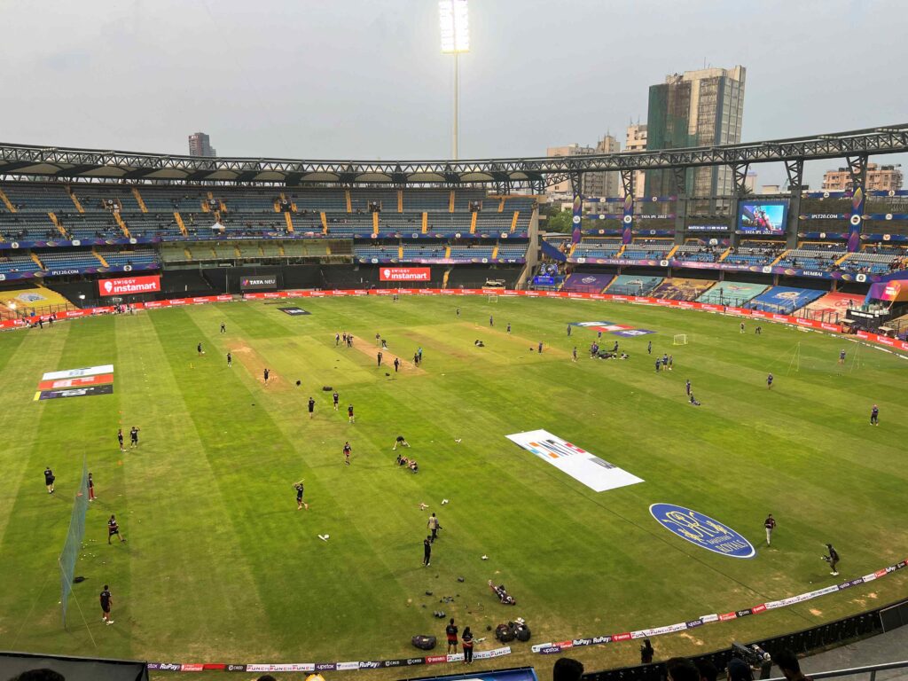 Wide shot of the inside of Wankhede Stadium with cricket players on the field warming up.