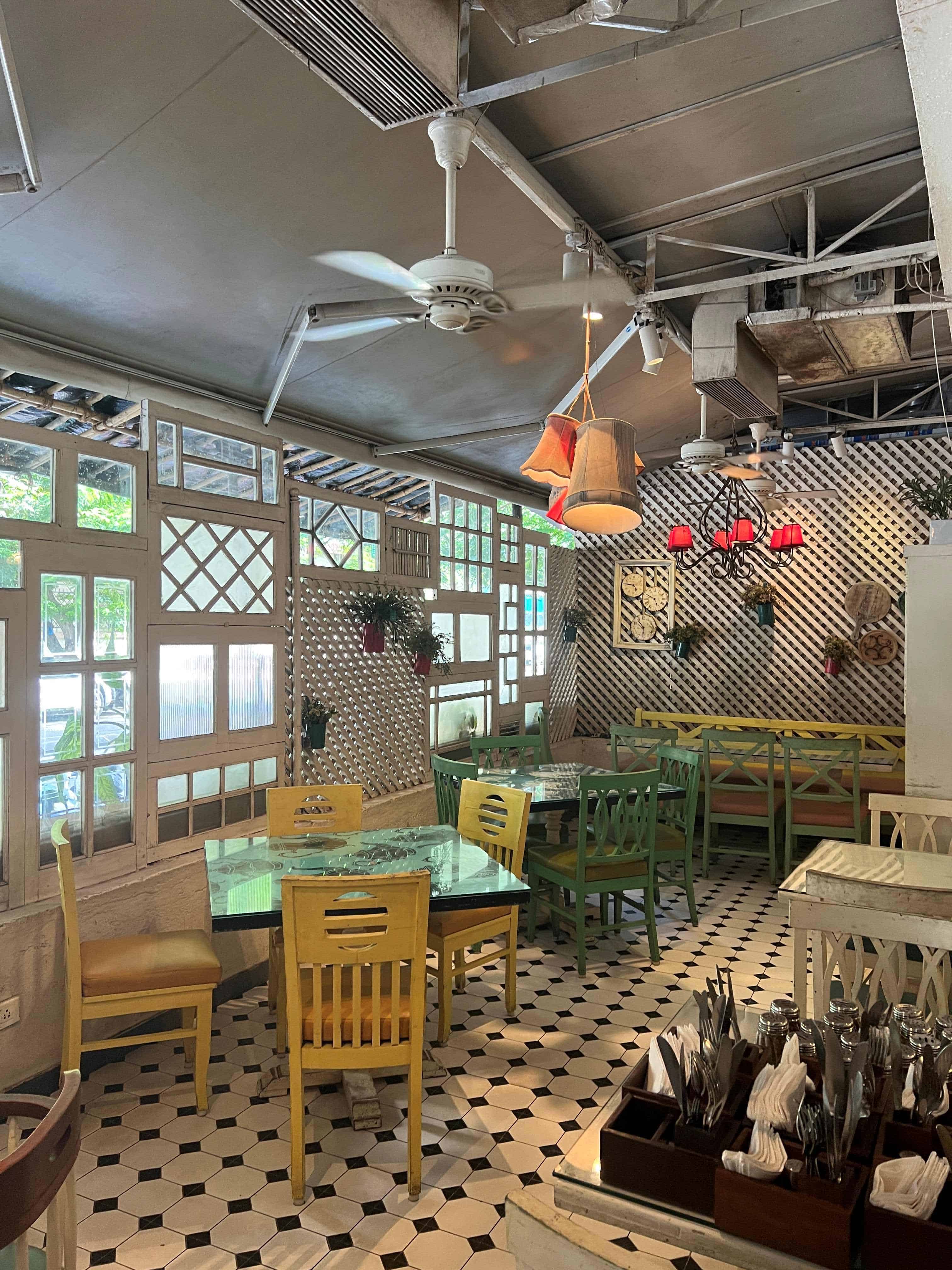 Interior of Fable restaurant in Juhu, with black and white checkered floor, and cute rustic wooden tables and white windows.