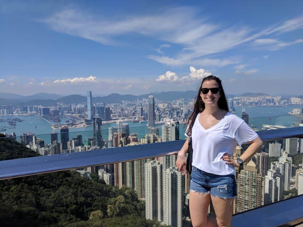 Girl standing at Victoria Peak in Hong Kong with the city skyline and bright blue sky in the background