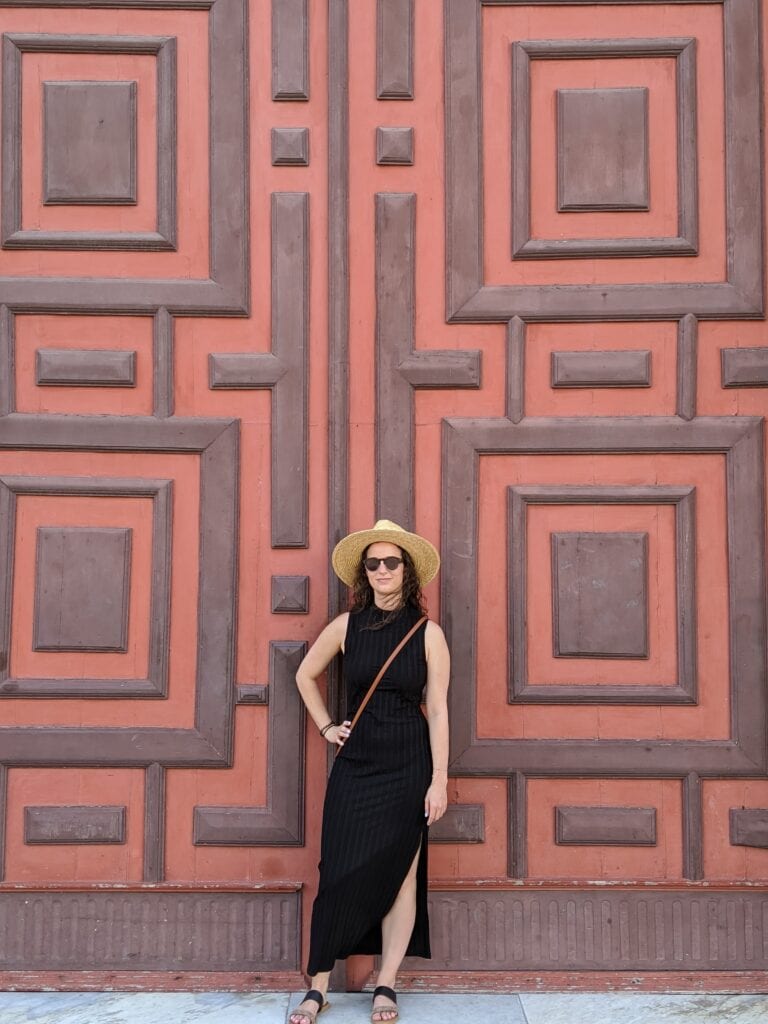 Girl in black dress standing in front of large door with red and brown pattern in Cartagena Colombia.