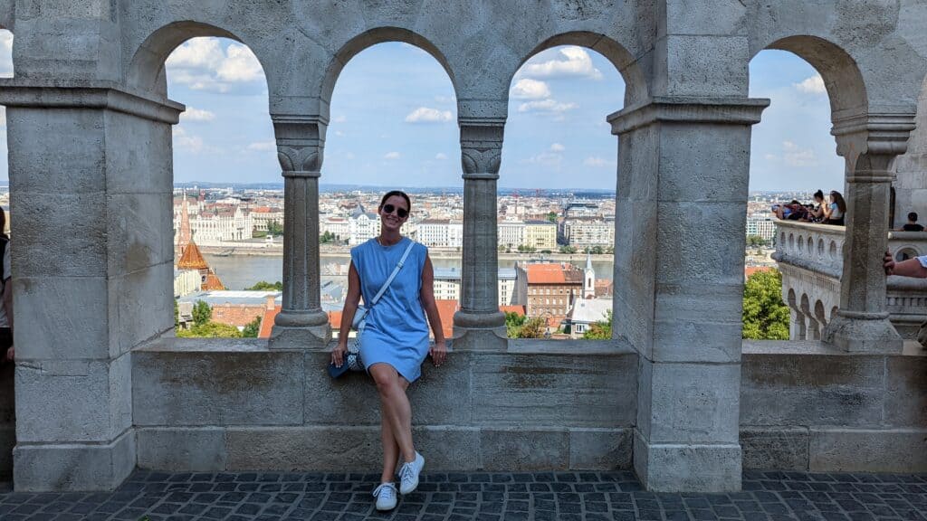 Girl in blue dress sitting on Fisherman's Bastion with the Budapest skyline in the background.