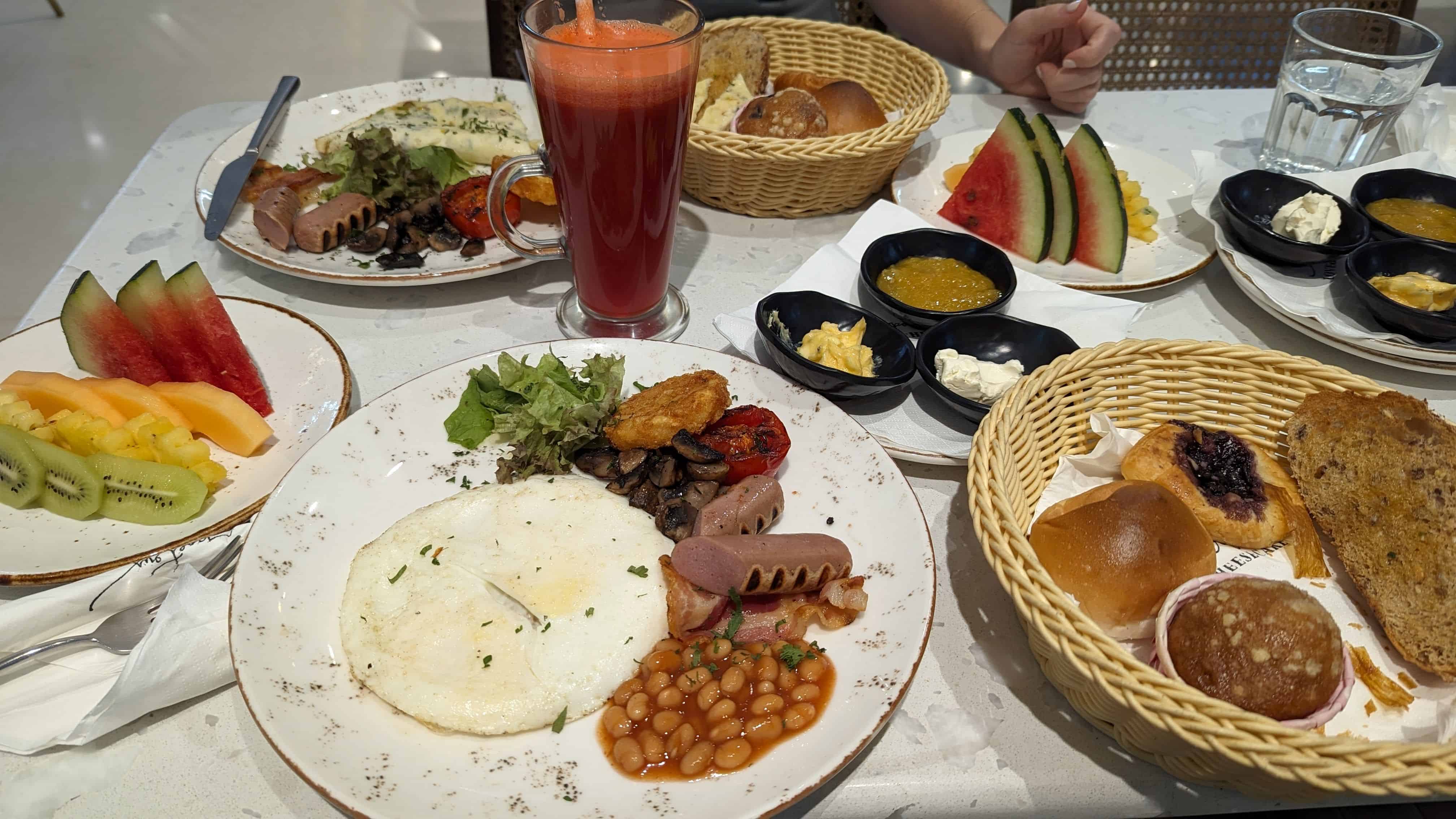 Table filled with breakfast dishes including eggs, beans, sausage, bacon, bread, and fruit at Poetry by Love and Cheesecake.