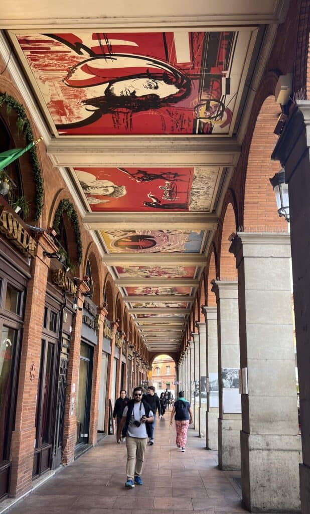 Ceilings with paintings of people and designs in a stone arched walkway in Toulouse, France.