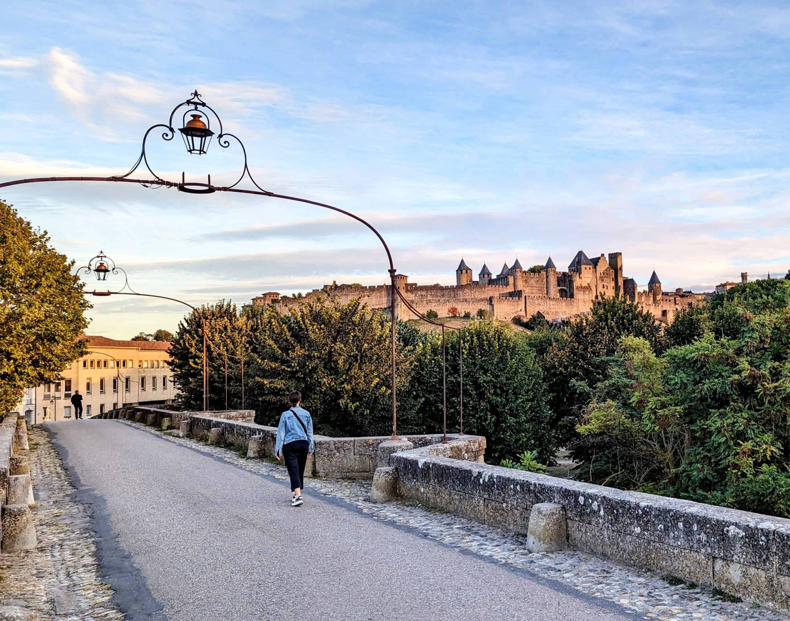 A girl walking across Pont Vieux bridge in Carcassonne, France with the walled city in the background.