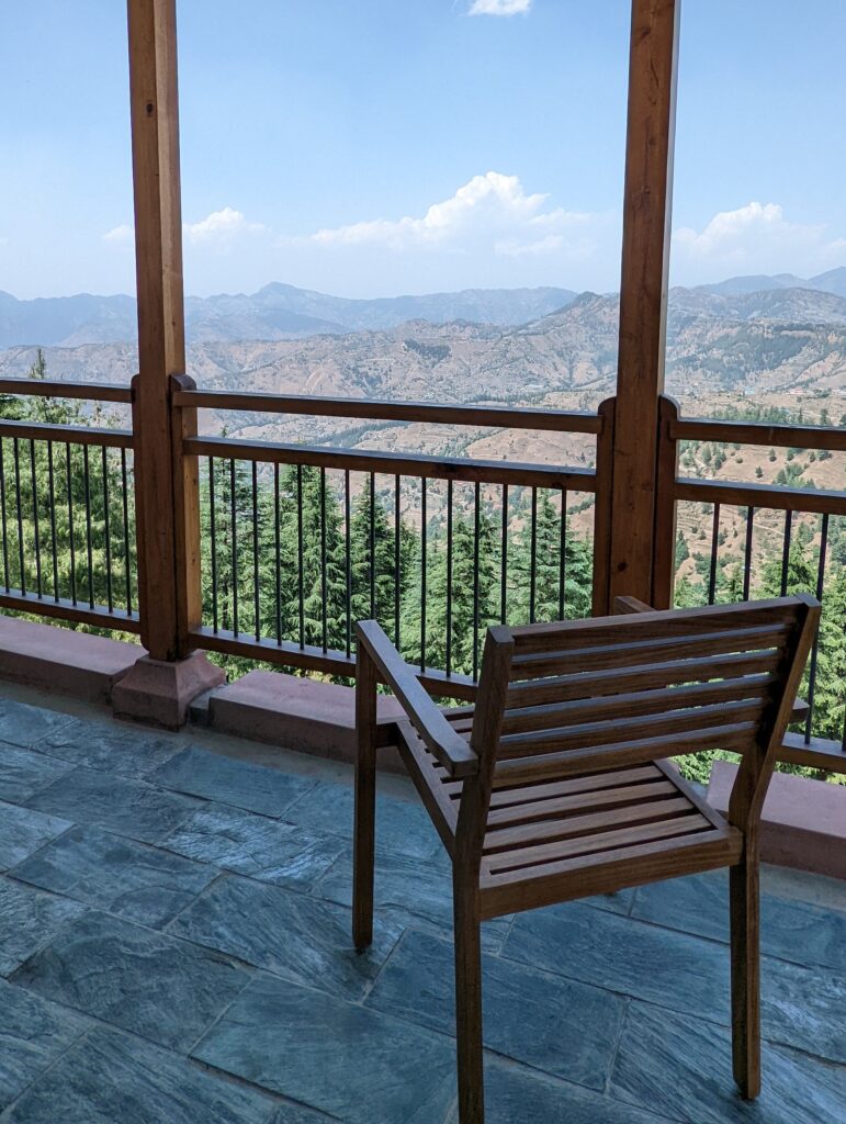 View from balcony of a room at Taj Theog with an empty chair and the Himalaya mountain peaks in the back.