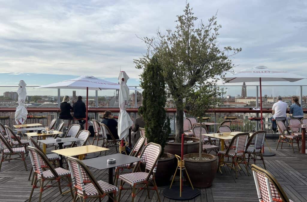 Rooftop bar in Toulouse with empty tables, umbrellas, and bar seating looking out over the city.