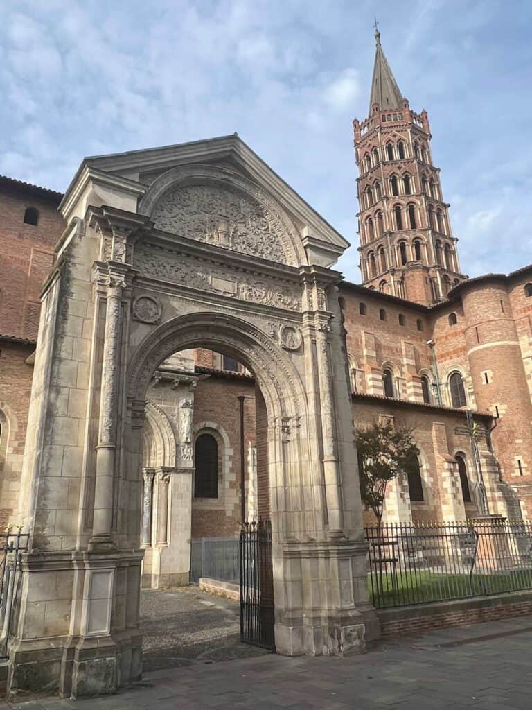 Arched stone entrance to Basilica Saint Sernin with tall spire in the background.