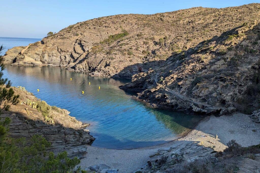 Overhead view of Cala sa Sabello beach in Cadaques Spain with stone beach and blue water cove that extends out to the ocean.