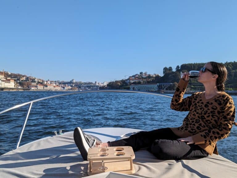 Girl sitting on the front of a small boat, drinking a glass of Porto on the Douro River on a blue sky day.