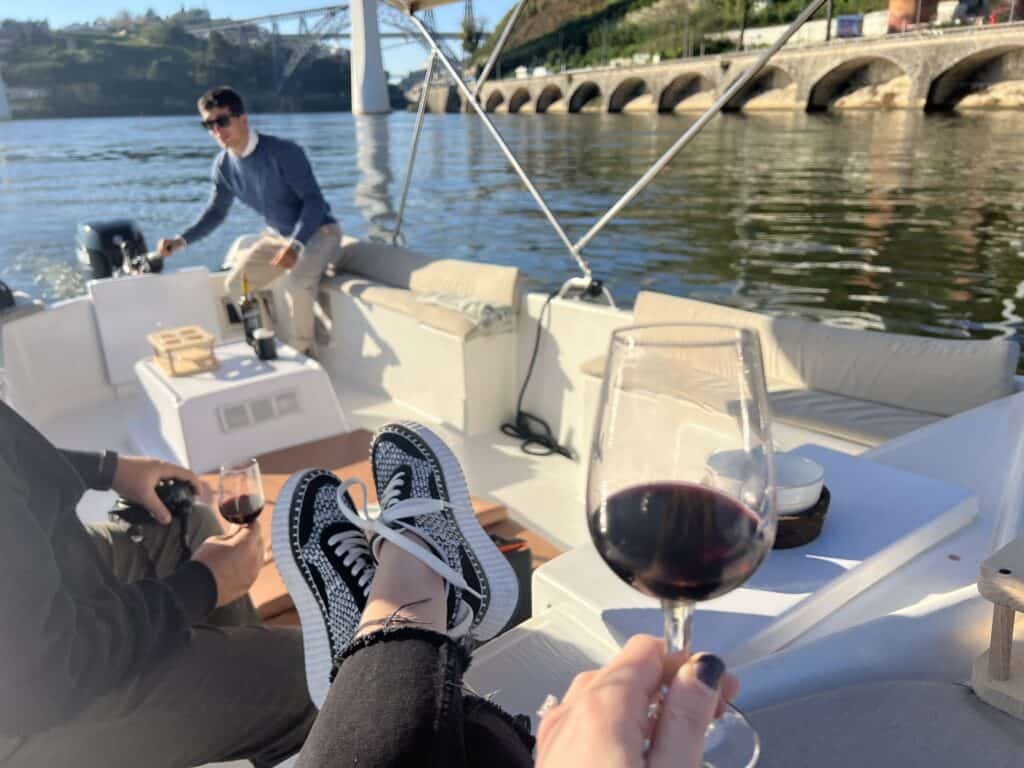 Interior of a small open boat on a sunny day in Porto, including  a couple people and a glass of Port wine.