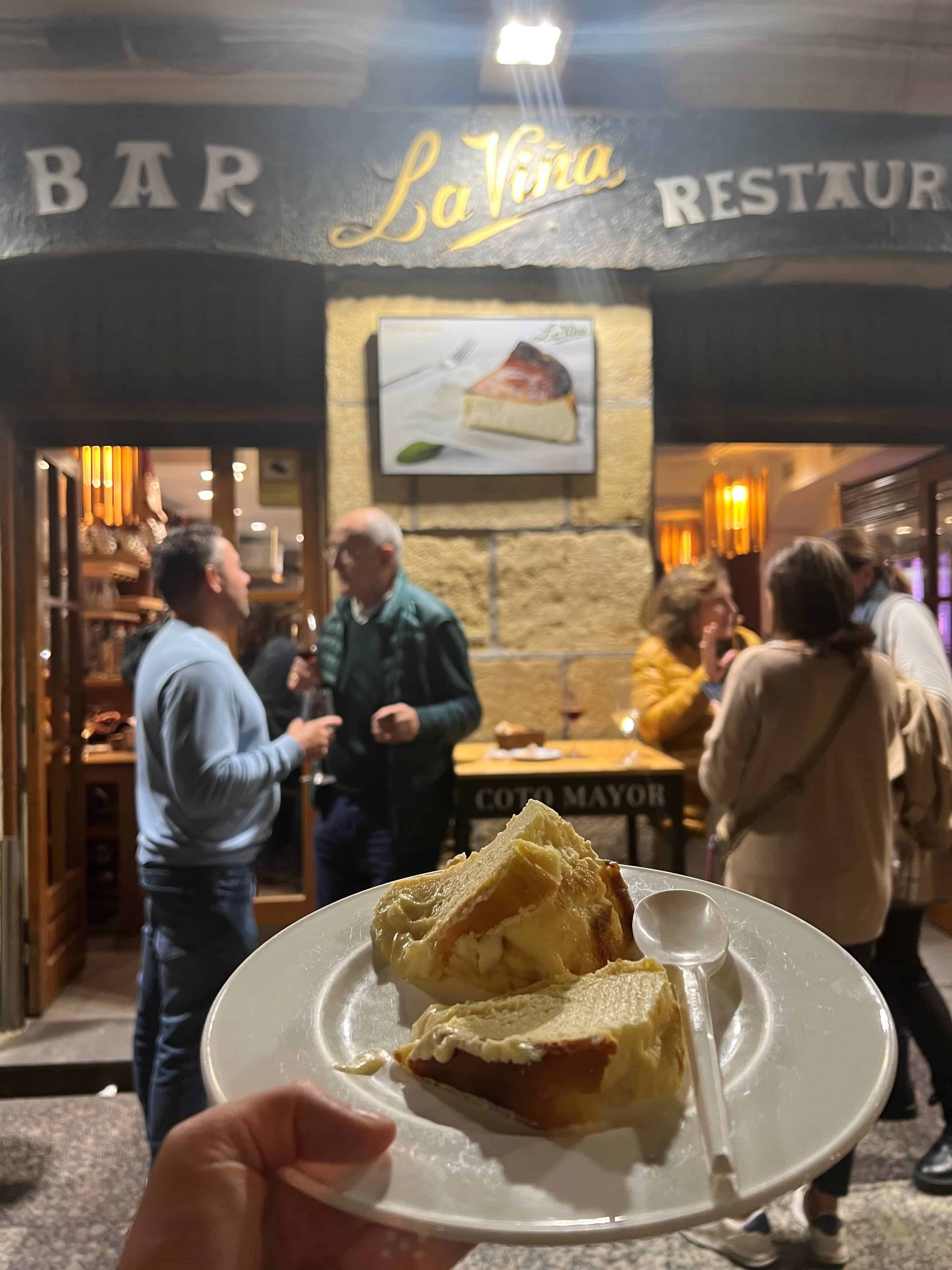 Close up of a plate of cheesecake held up in front of the restaurant La Vina in San Sebastian.