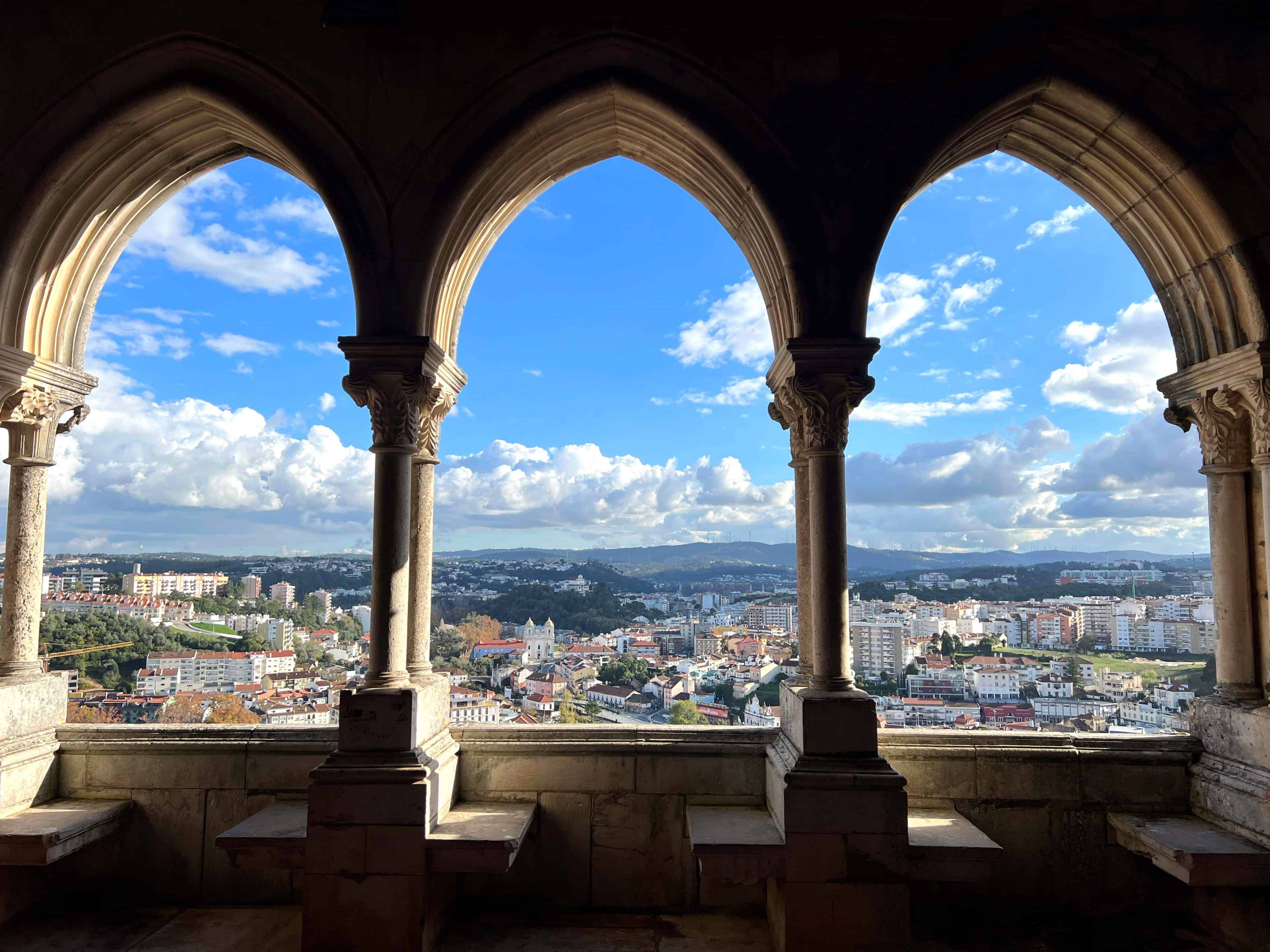 View from inside Leiria Castle showing 3 arched windows looking out over the city of Leiria and its blue sky.