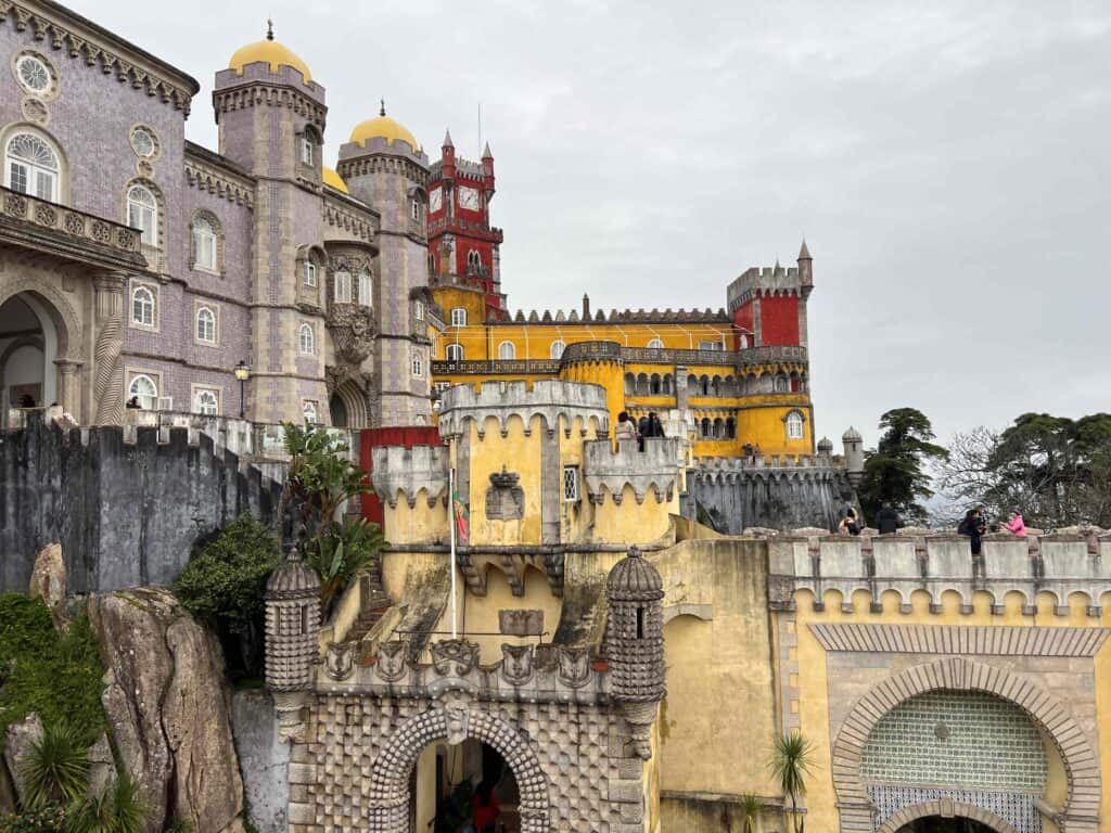 Front view of Pena Palace in Sintra with purple, yellow, and red stone sections and turrets. 