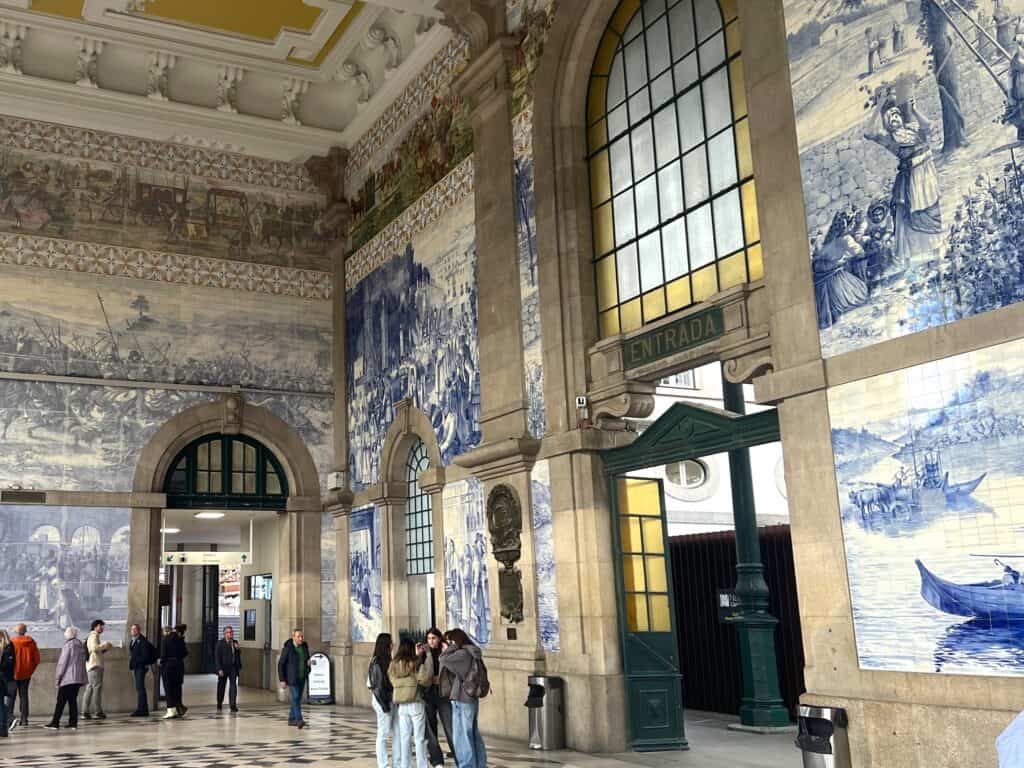 Inside of Sao Bento train station in Porto, showing the blue and white painted tiles the cover the tall walls and the tall archways to the tracks.