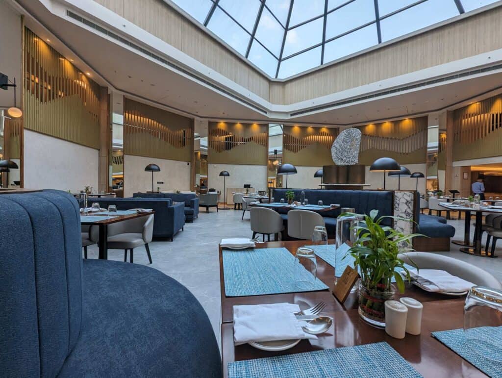 Empty restaurant with blue couches and wooden tables with place settings inside the Taj Vivanta hotel in Shillong.