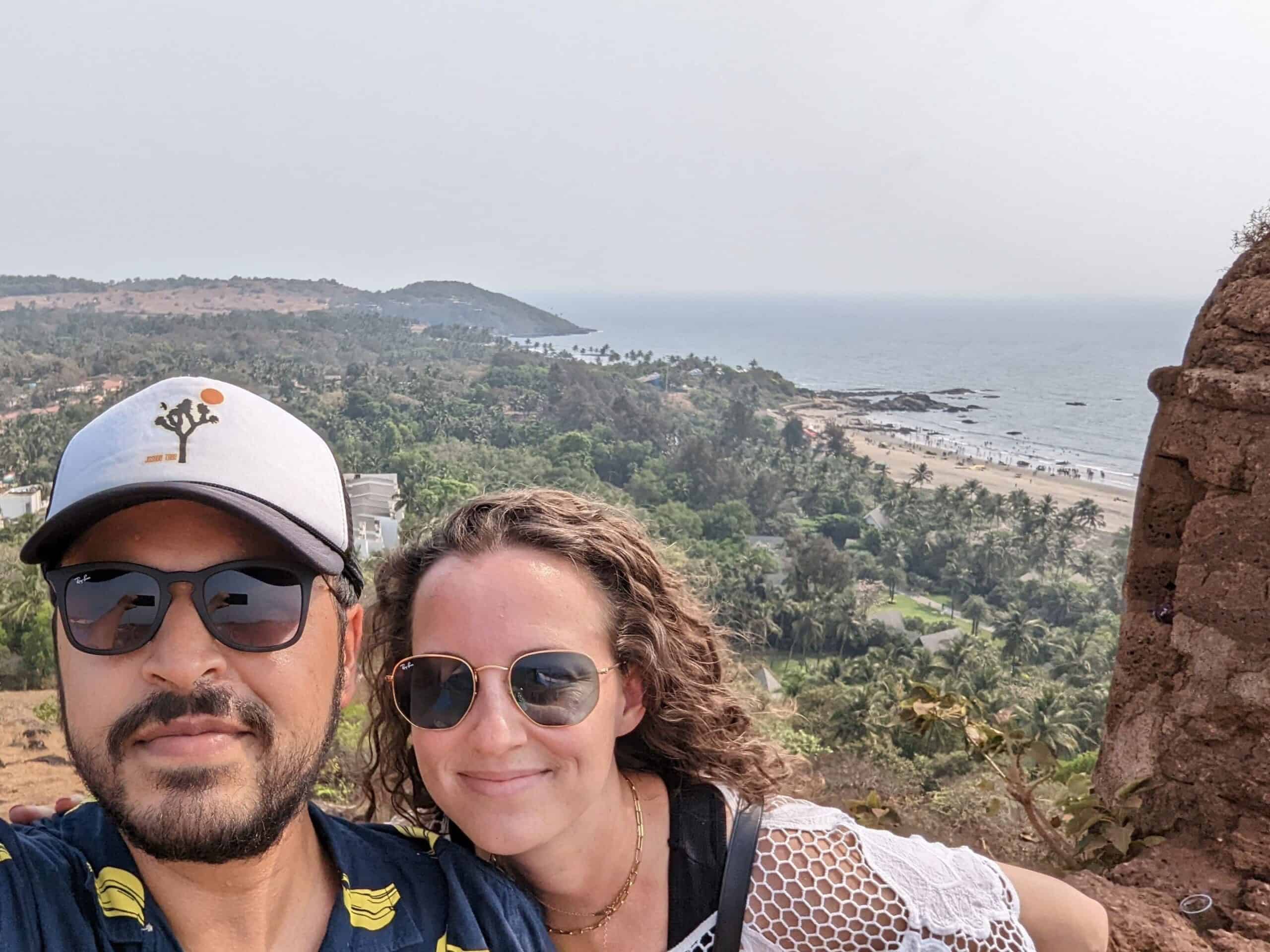 A couple standing at the top of Chapora Fort in Goa with views of the beach and the ocean beyond it.