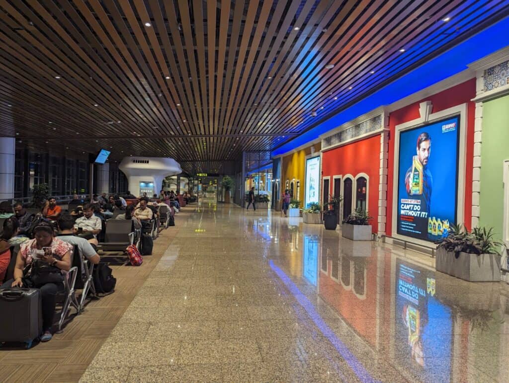 Waiting area in Mopa Airport in Goa with people sitting on the left in chairs and an open tiled walkway on the right.