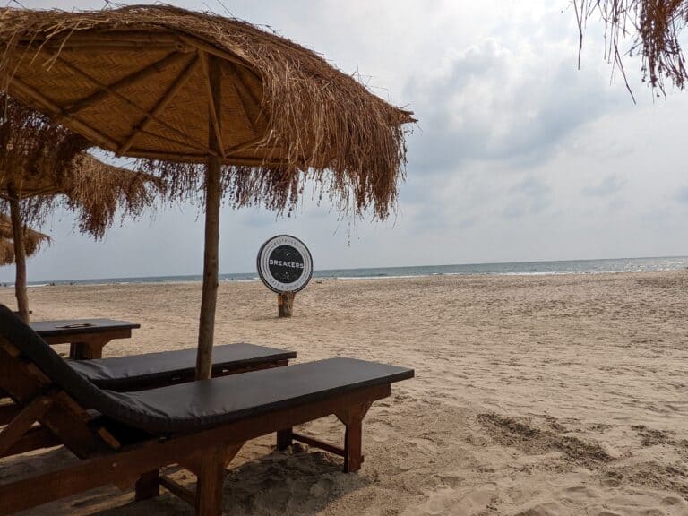 Empty beach loungers with straw umbrellas on Ashvem Beach in Goa.