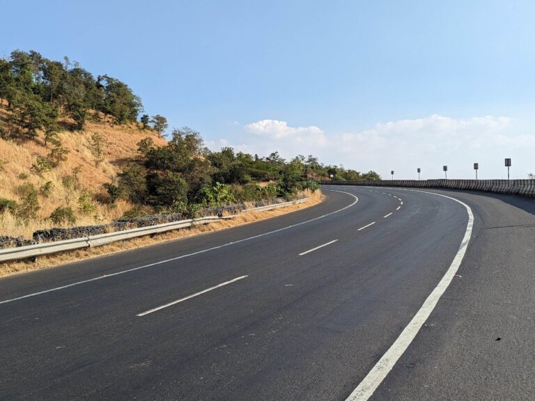 The curve of an empty highway road with a small hill on the left and the blue sky above it.