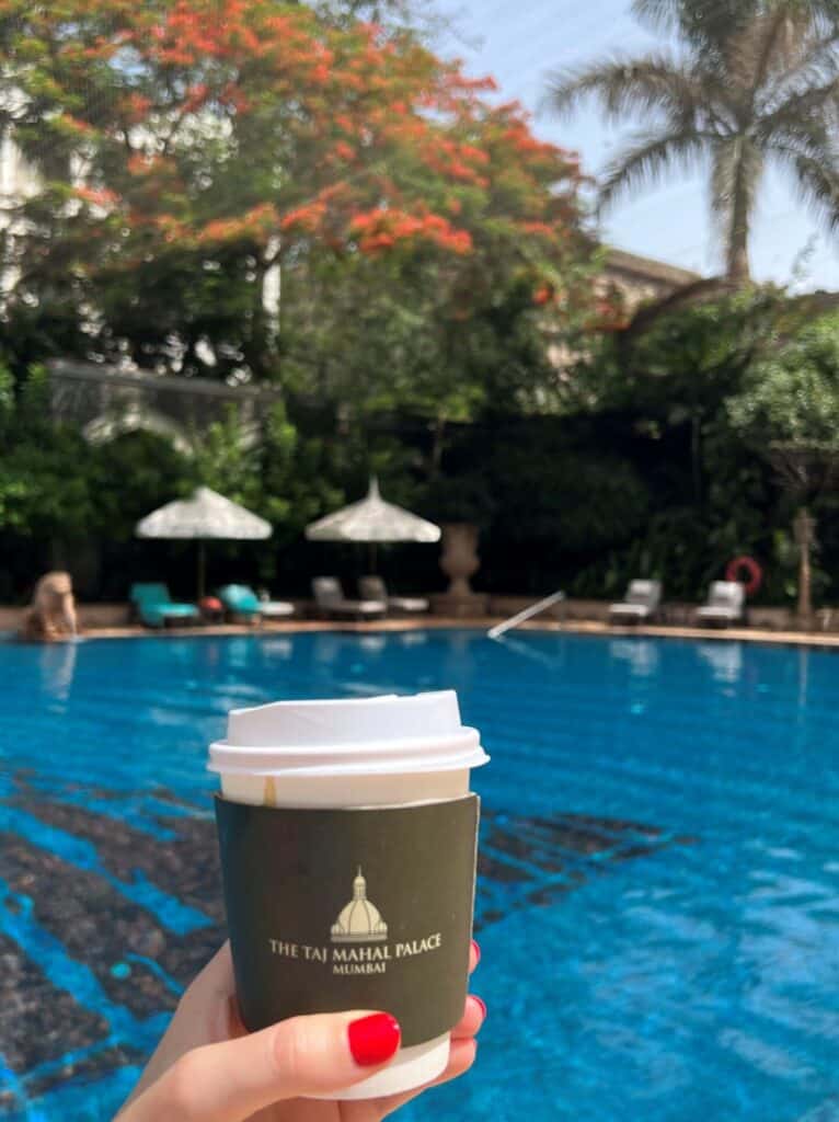 View of the Taj Mahal Palace pool with a girl's hand holding a coffee cup in front of it.