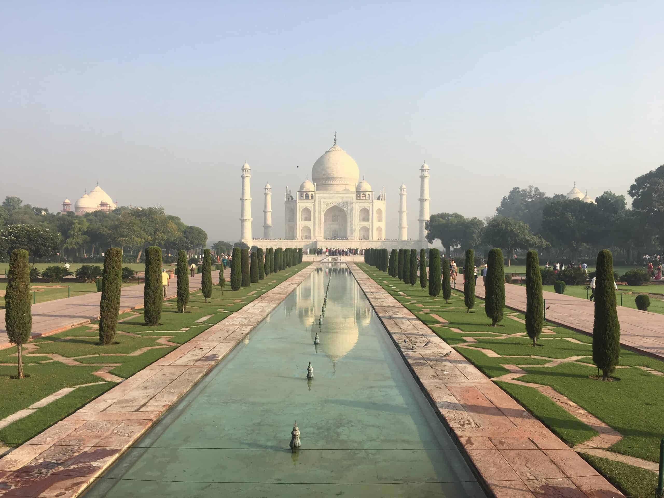 View of the Taj Mahal on a clear sunny day from the entrance to the gardens with the long reflecting pool as the focal point in the center of the image.