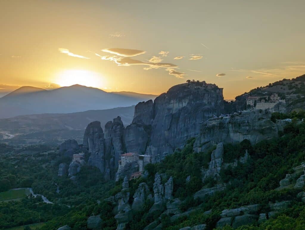 Sunset view of monastery in Meteora from the main observation point with the sun setting behind the mountain.