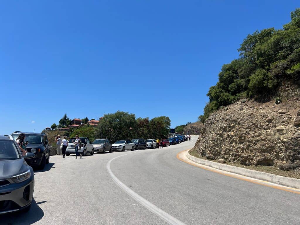 Curve of the road in Meteora that leads up to the Great Meteoron Monastery with cars parked alongside the road.