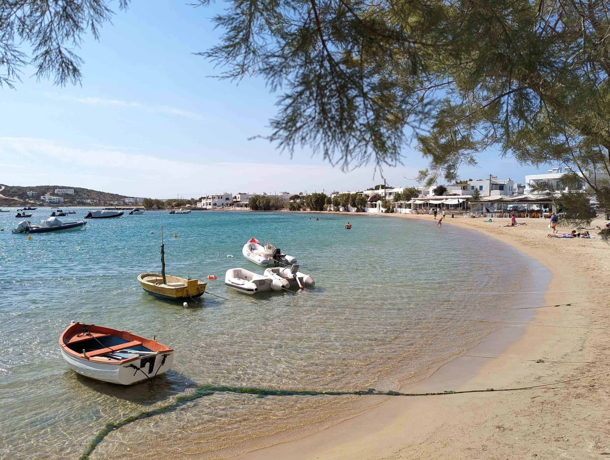 View of small sandy beach in Aliki on Paros with four small boats anchored a small distance off shore in the clear light blue sea water.