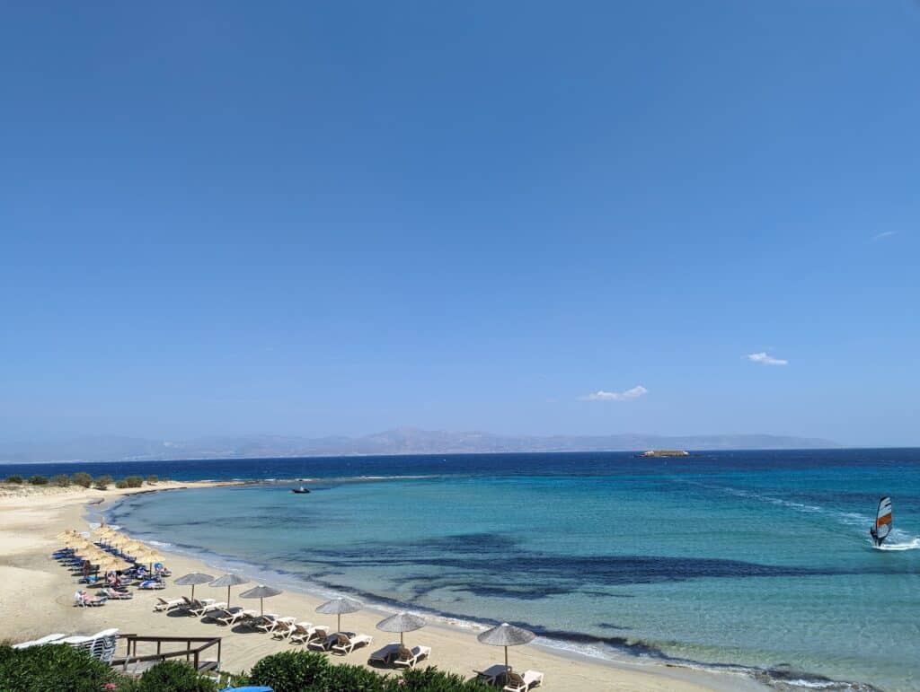 View of Sandy beachfront with a few lounge chairs and light blue water fading into deep blue sea.