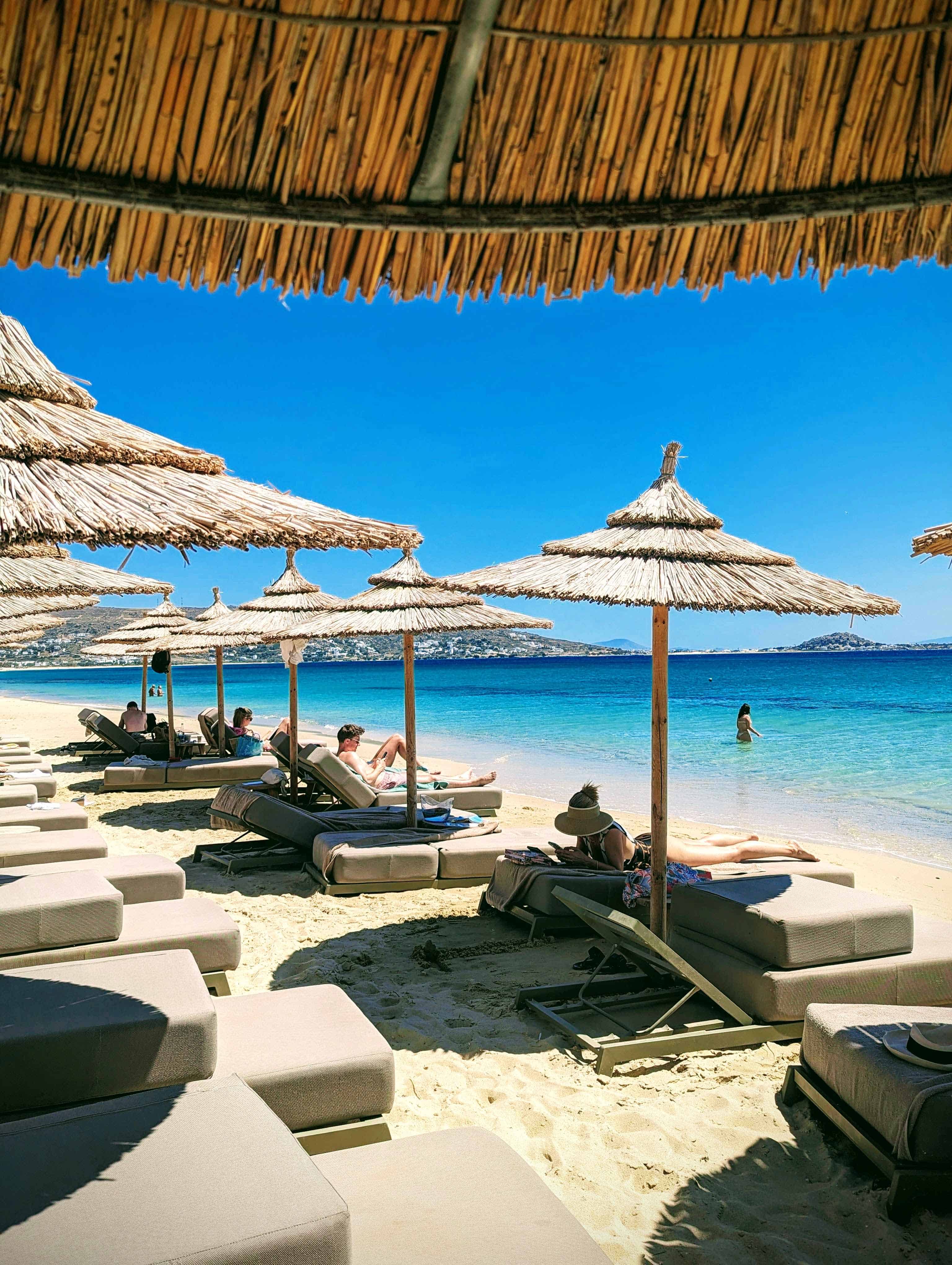 View of beach loungers with individual thatched umbrellas at Sundunes beach club with a sandy beach and light blue sea water.