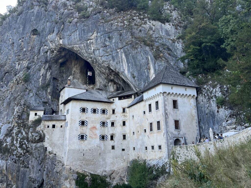 Predjama castle from the front, showcasing the medieval castle and how it is built into the rocky cliffside behind it.