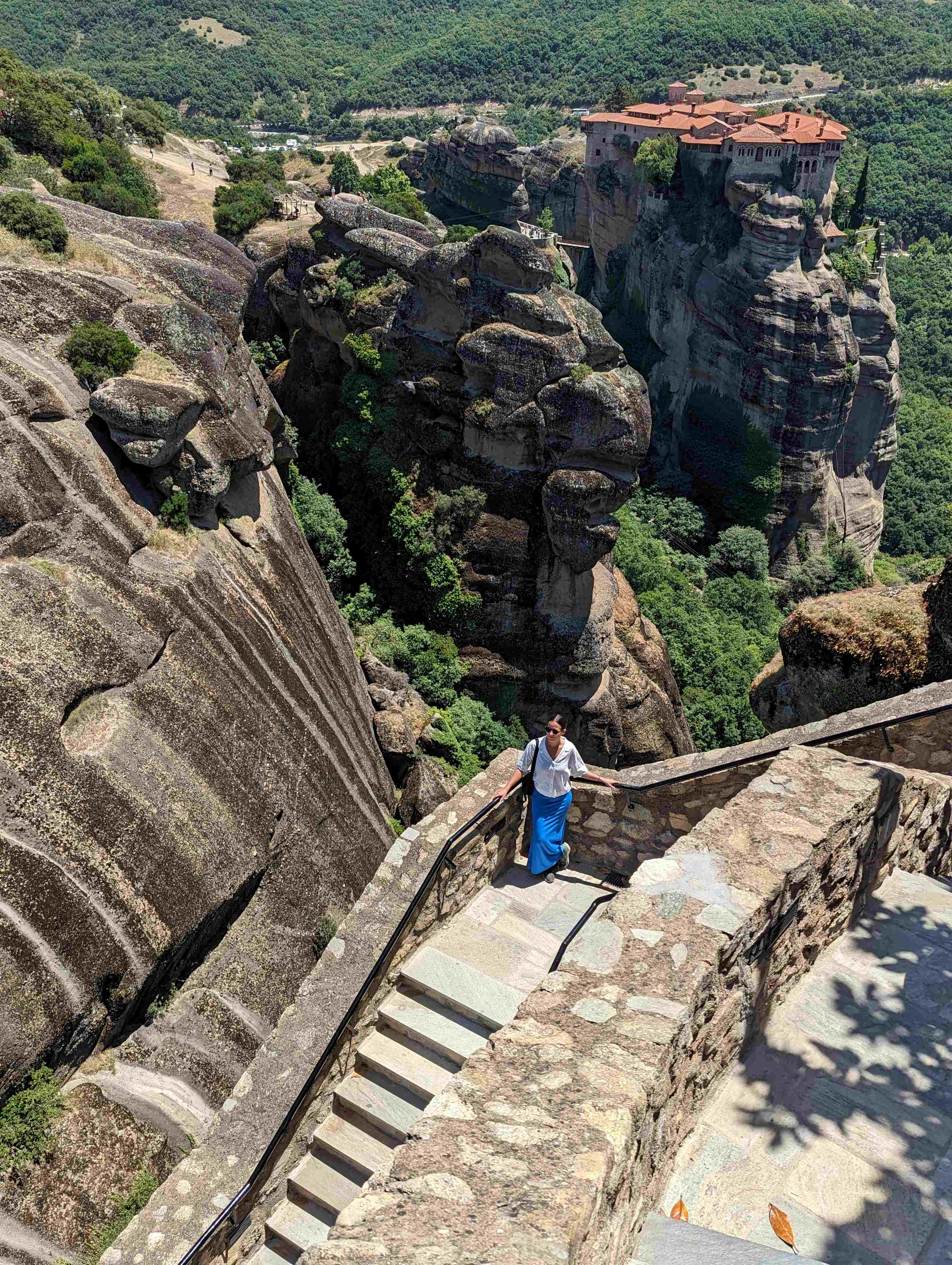 View from above of the steps at the entrance of Holy Monastery of the Great Meteoron with another Monastary perched atop a towering rock formation in the background.