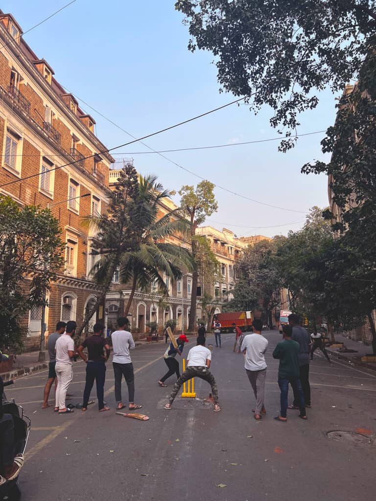 People playing street Cricket in the historic Ballard Estate neighborhood in Mumbai. You can see colonial style buildings lining the street as well. 